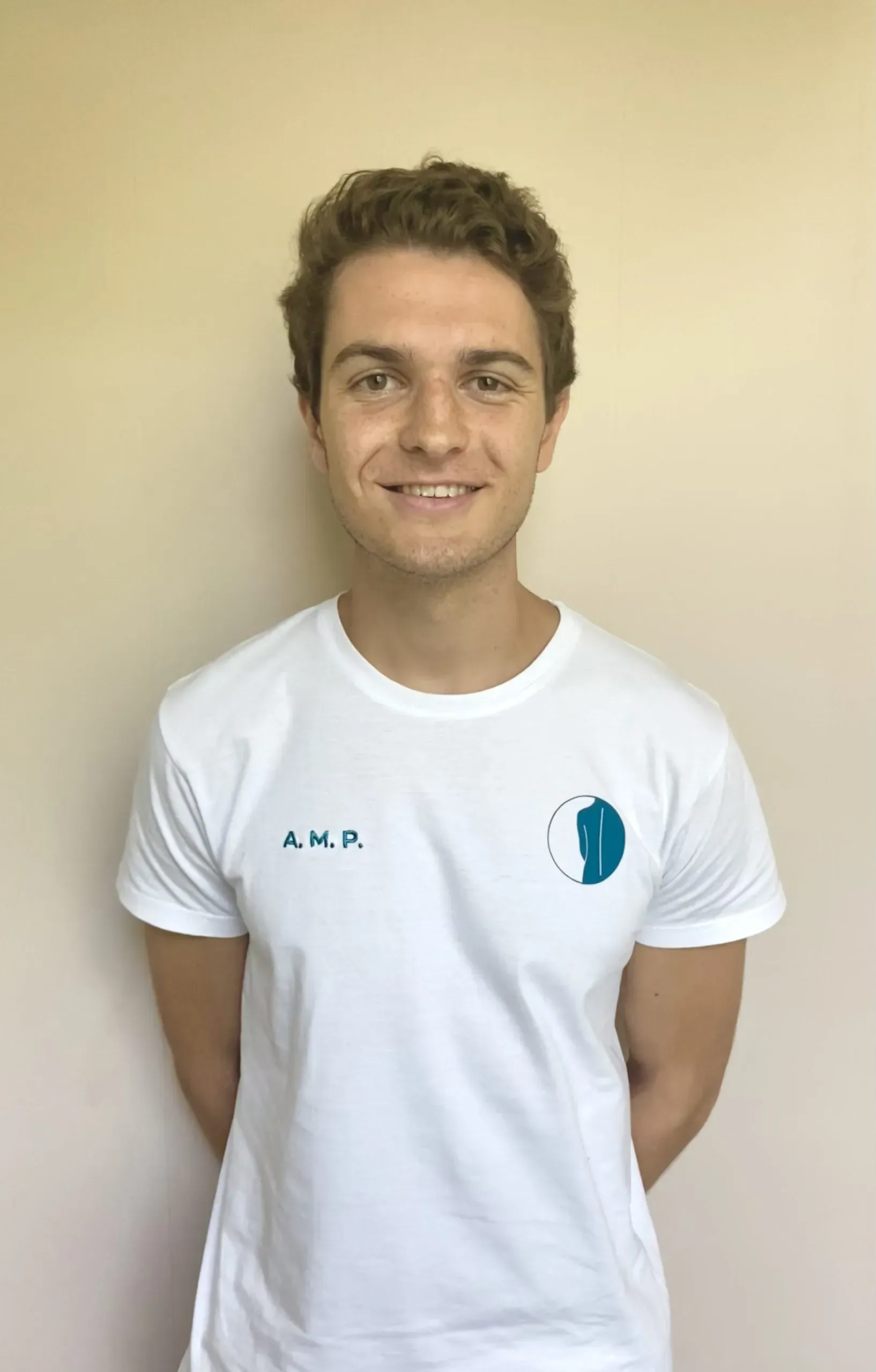 Una persona joven con cabello castaño rizado, que viste una camiseta blanca con un pequeño logotipo.