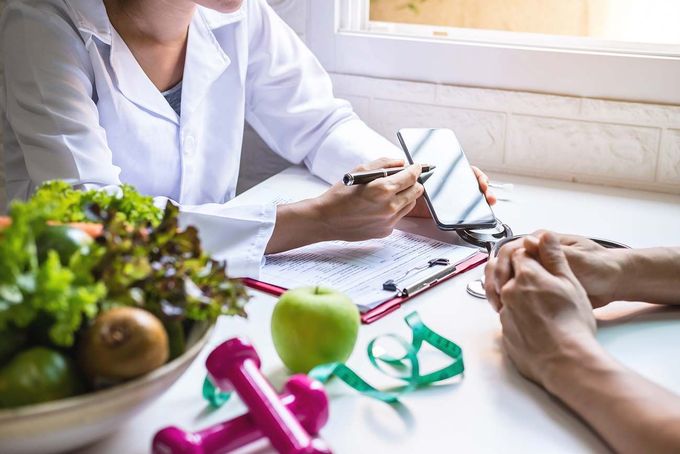 Nutricionista conversando sobre un plan de alimentación con un cliente en una mesa con frutas, verduras y pesas.