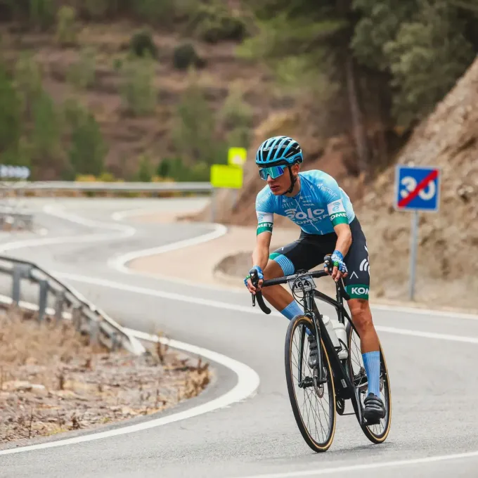 Un ciclista con maillot azul de su equipo y casco recorre en bicicleta una sinuosa carretera de montaña 