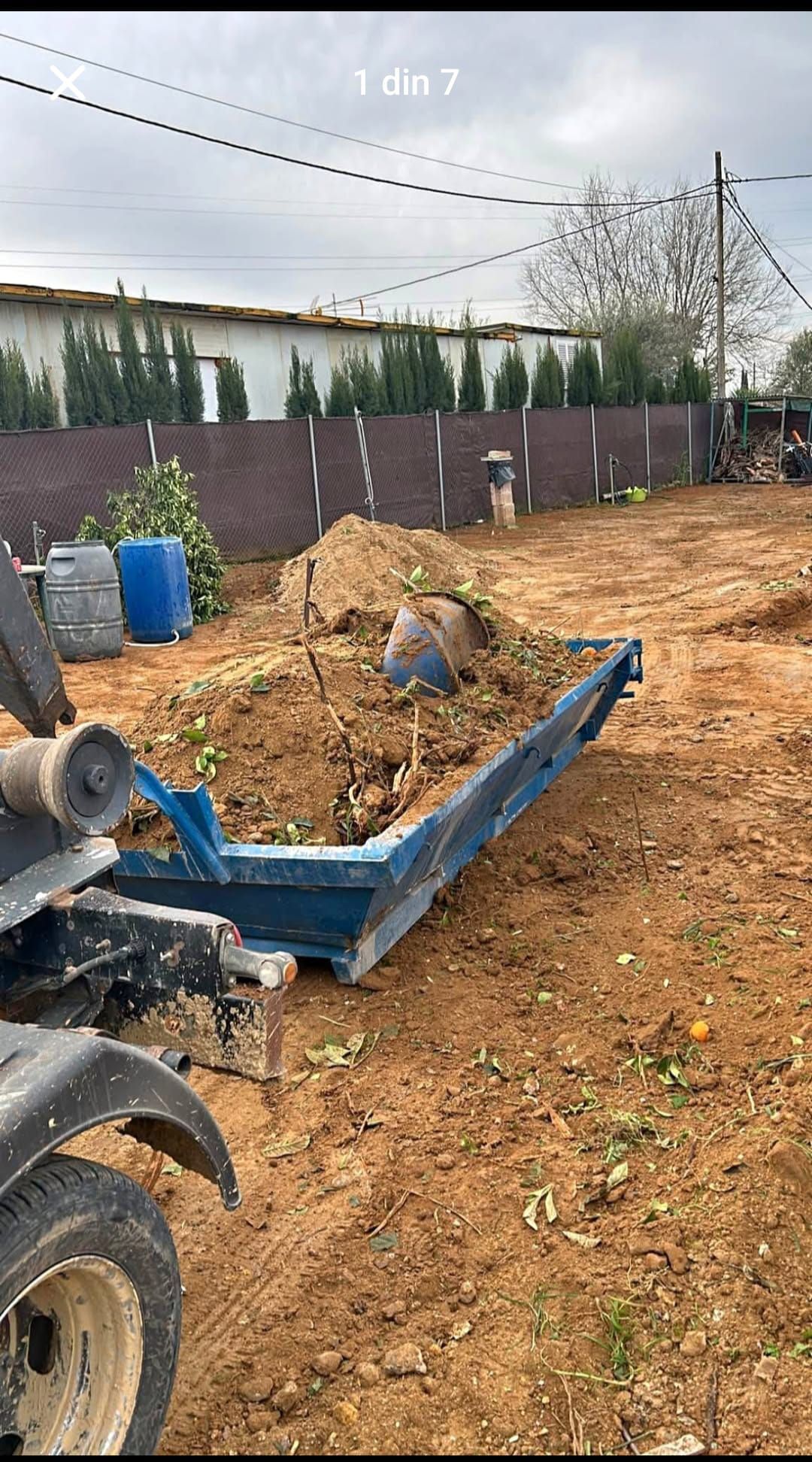 Un contenedor de basura azul está en el medio de un campo de tierra.