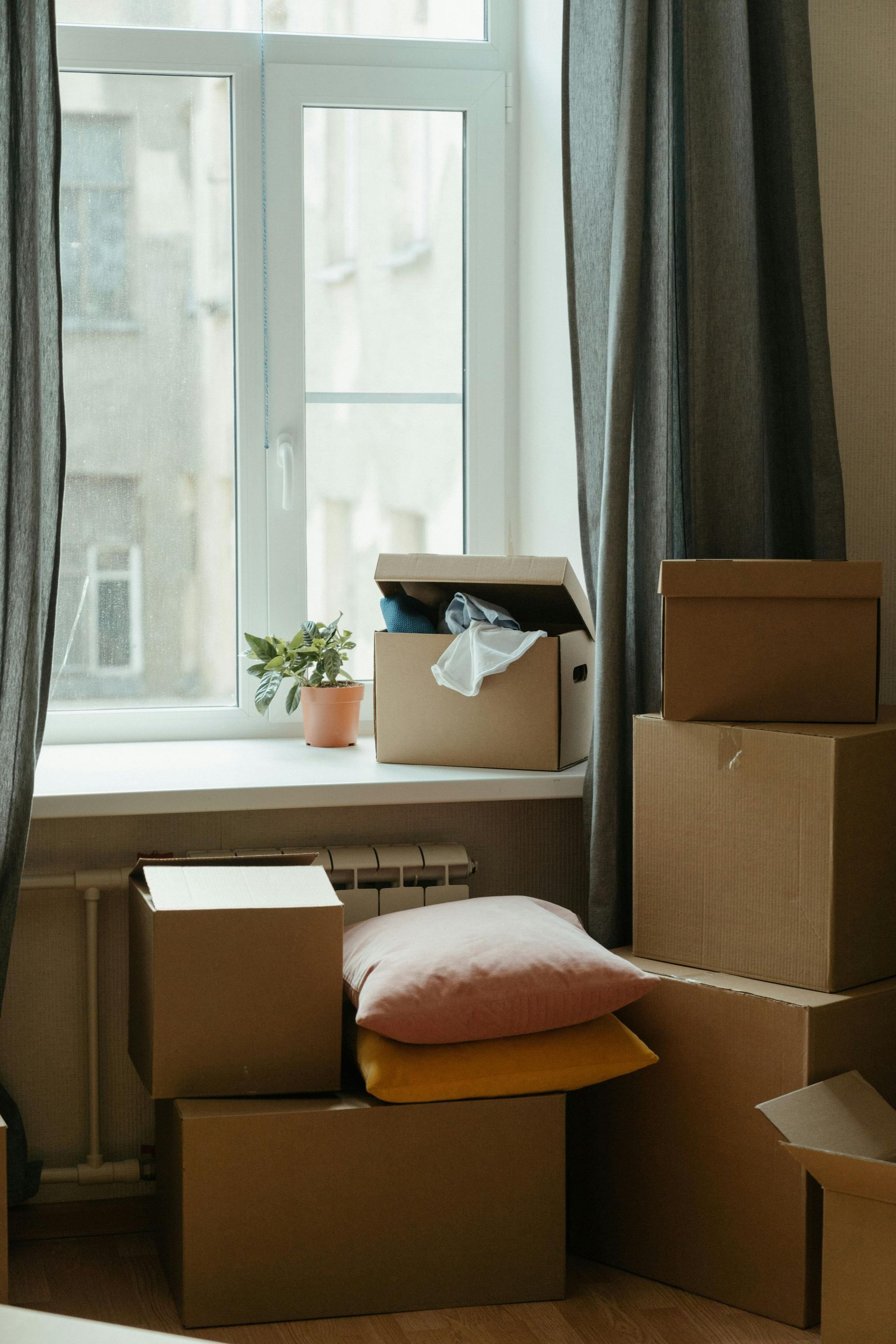 Una habitación llena de cajas de cartón y almohadas junto a una ventana.