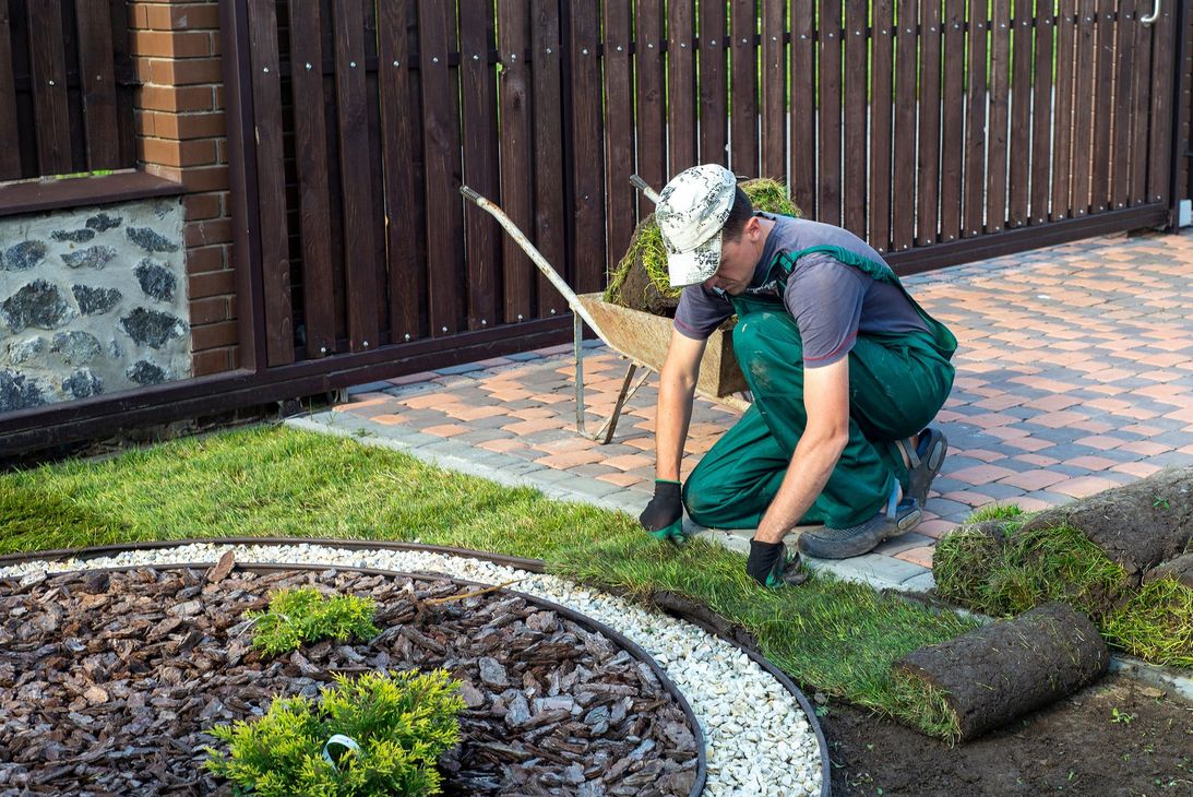 Jardinier agenouillé pour tailler la pelouse le long d'un parterre de jardin incurvé, à côté d'une allée pavée