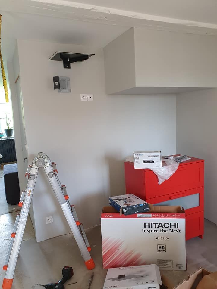 Pièce avec échelle, murs gris, armoire rouge, boîtiers de projecteur et appareils fixés au mur.