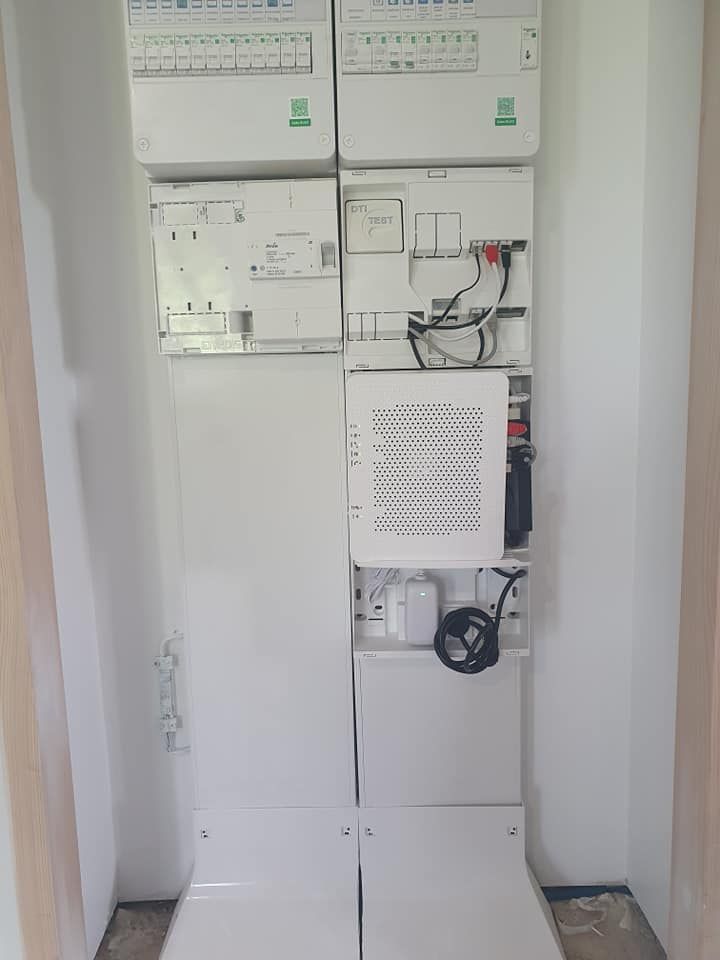 Boîtes électriques blanches empilées sur le mur. Elles contiennent des fusibles et un appareil ressemblant à un modem.