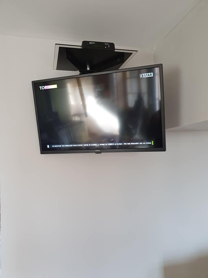 Un téléviseur à écran plat fixé sur un mur blanc, incliné vers le bas depuis un support pivotant fixé au plafond.