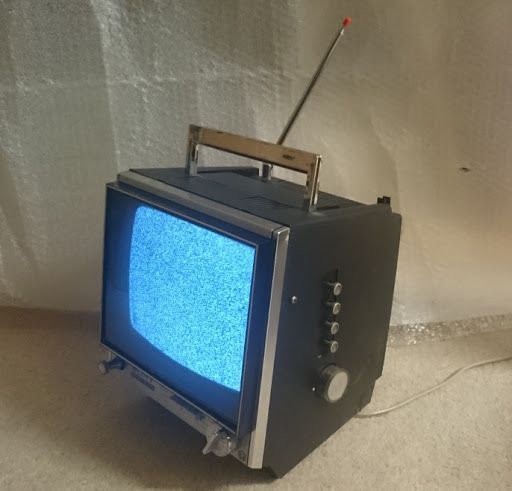 Téléviseur portable vintage noir et argent avec antenne, affichant un écran statique.