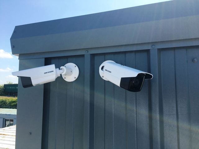 Deux caméras de sécurité blanches, montées sur une structure métallique grise, capturent la vue extérieure.