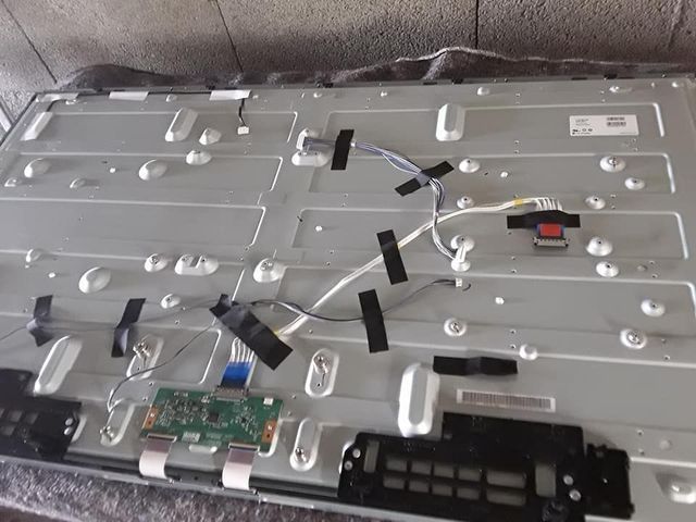 Arrière d'un téléviseur démonté, avec composants électroniques et câblage, fixés par du ruban adhésif sur un panneau métallique.