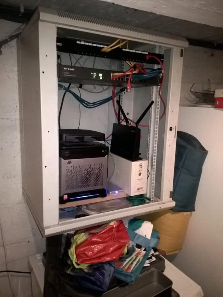 Baie de serveurs avec équipements réseau fixés au mur, câbles et périphériques de stockage.