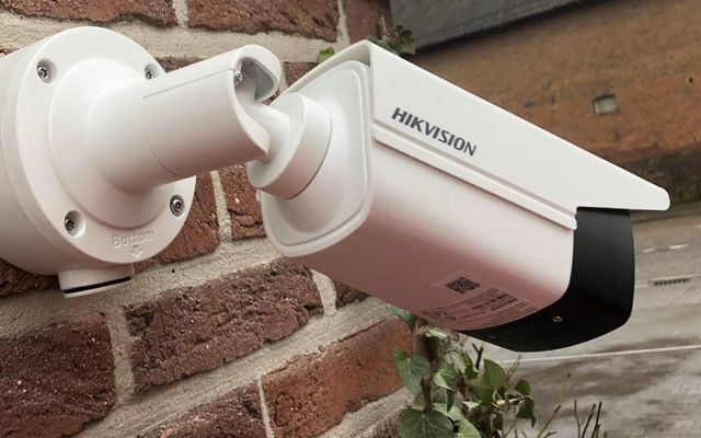 Caméra de sécurité Hikvision blanche fixée sur un mur de briques, légèrement inclinée vers le bas.