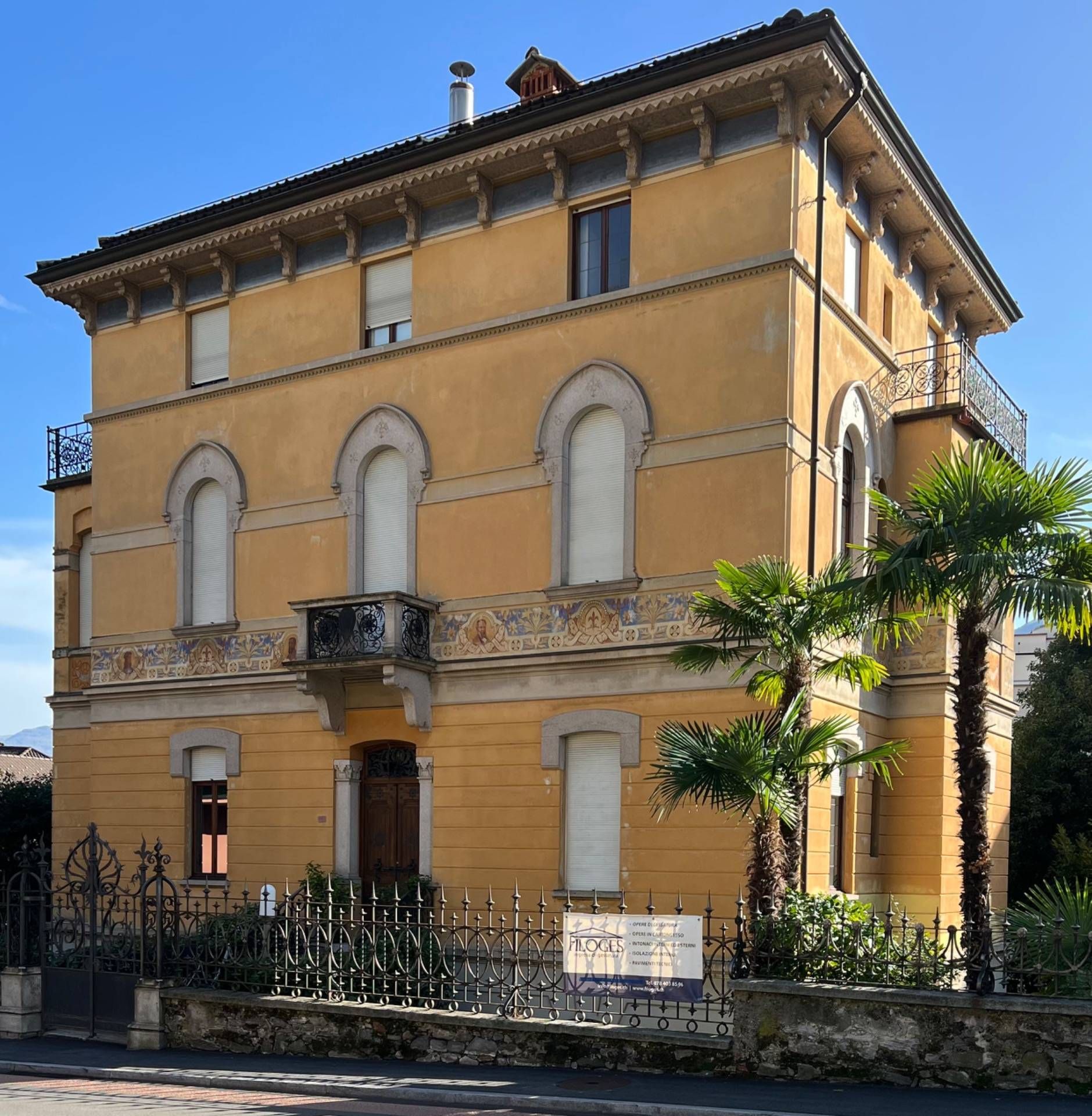 Un grande edificio giallo con una palma di fronte