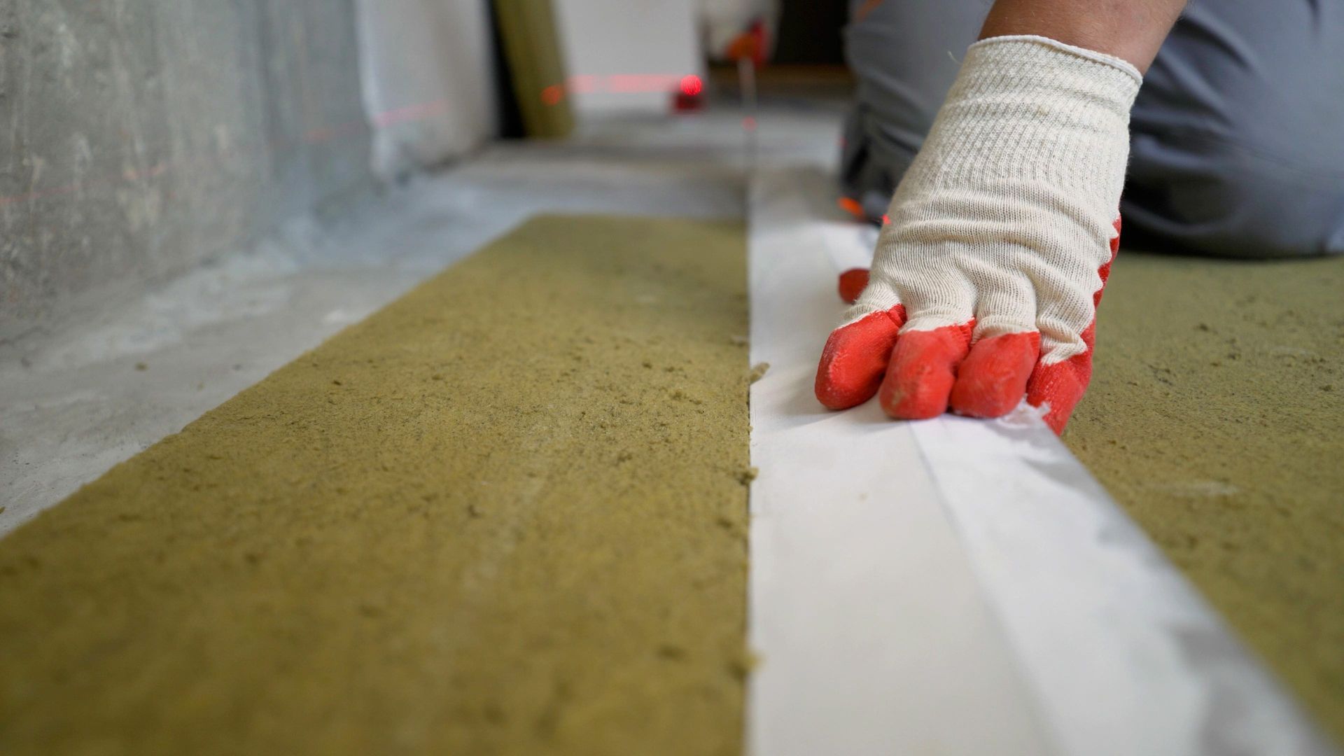 Une personne portant des gants rouges pose un isolant.
