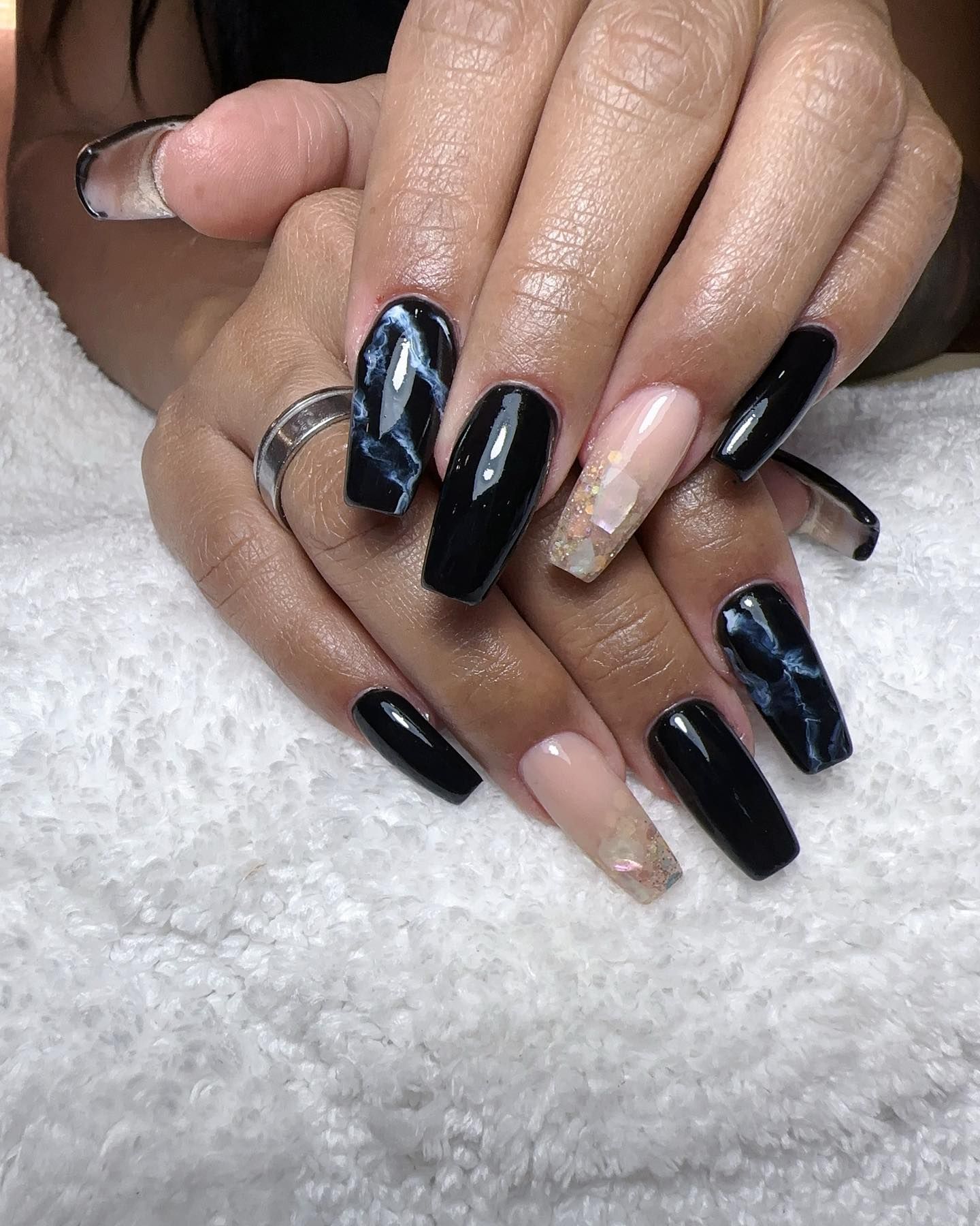 Manos con uñas largas en forma de ataúd. Diseños en negro, nude y mármol. Descansan sobre una toalla blanca.