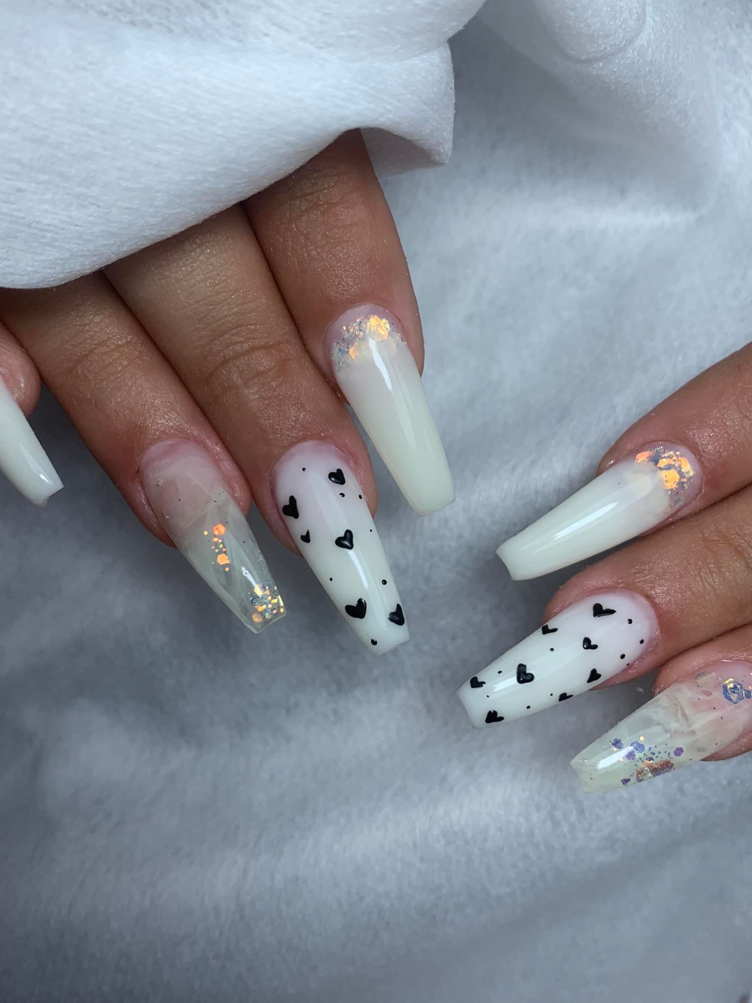 Uñas acrílicas largas de color blanco con detalles de corazones negros y brillo.