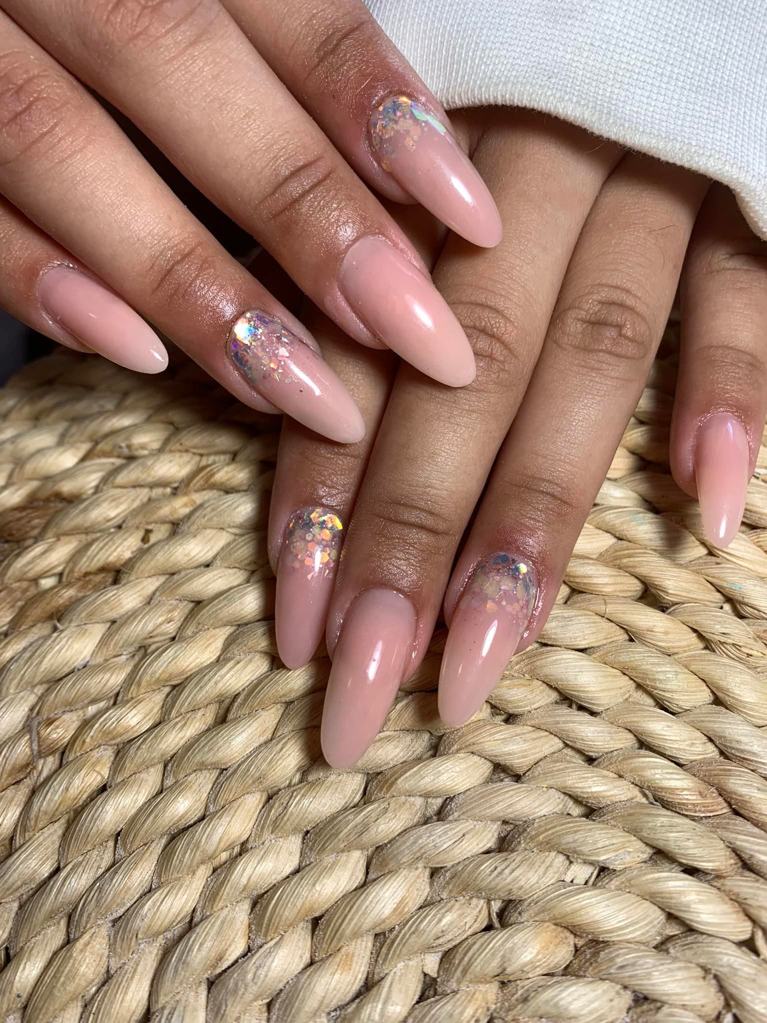 Las manos de una persona con uñas largas, en forma de almendra y pintadas de rosa, algunas con detalles brillantes, descansando sobre una superficie tejida.