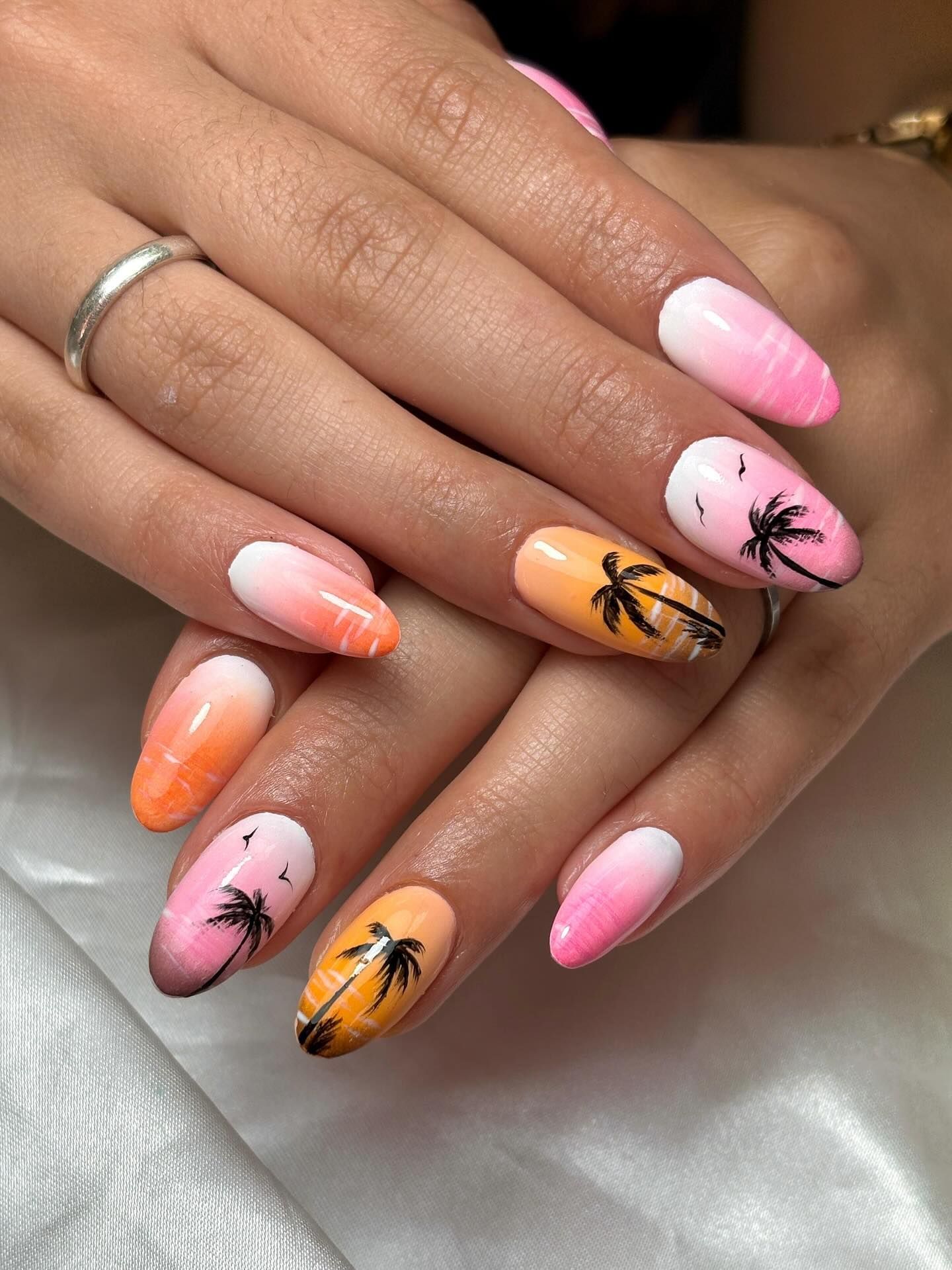 Uñas de mujer pintadas con colores ombre de atardecer y diseños de palmeras negras.