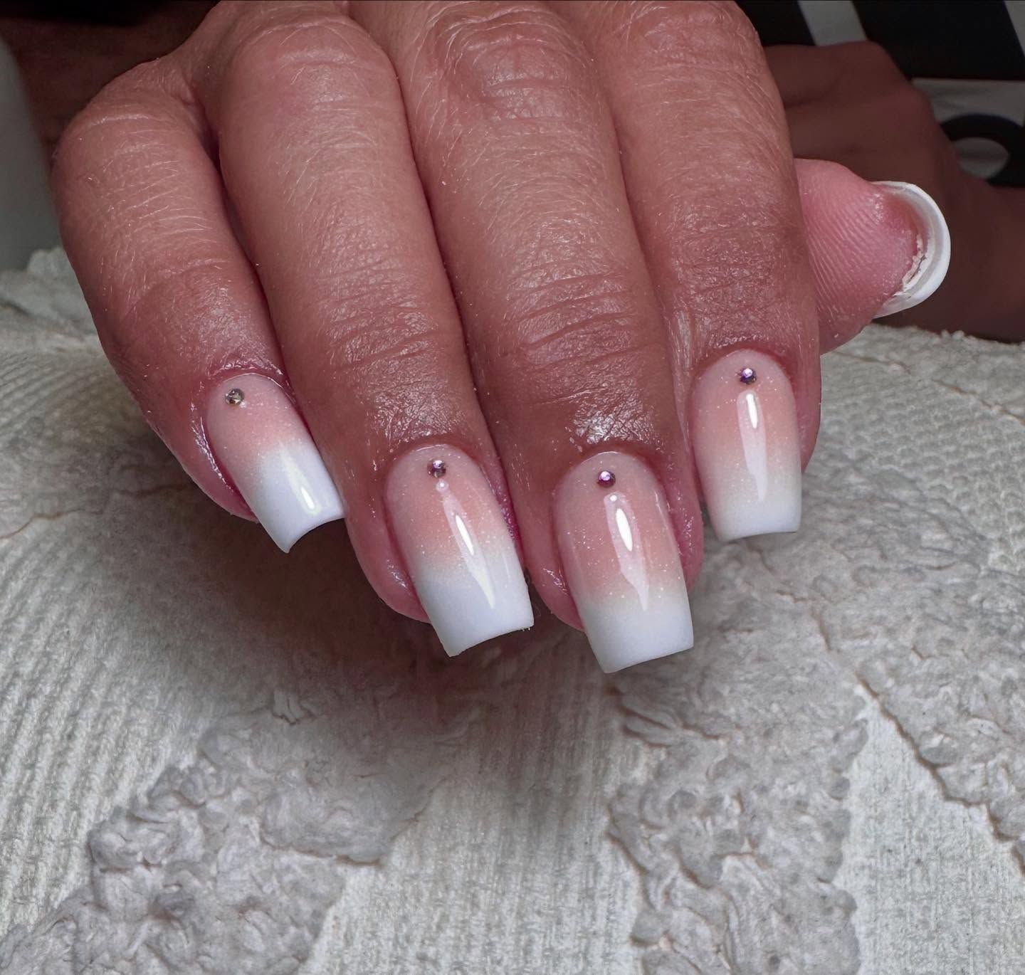 Uñas de forma cuadrada con efecto ombré, que pasa del rosa pálido al blanco, adornadas con pequeños diamantes de imitación.