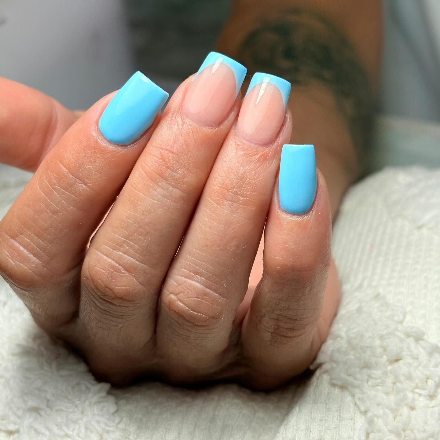 Mano con uñas acrílicas azules de forma cuadrada, una de ellas con punta francesa.
