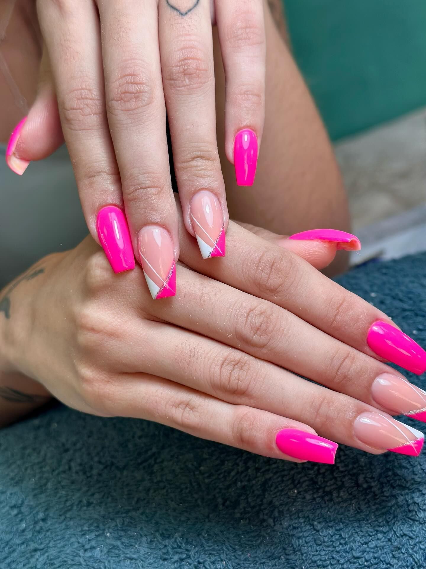 Manos con uñas de color rosa brillante y punta francesa en forma de ataúd. Una uña presenta un diseño diagonal blanco.