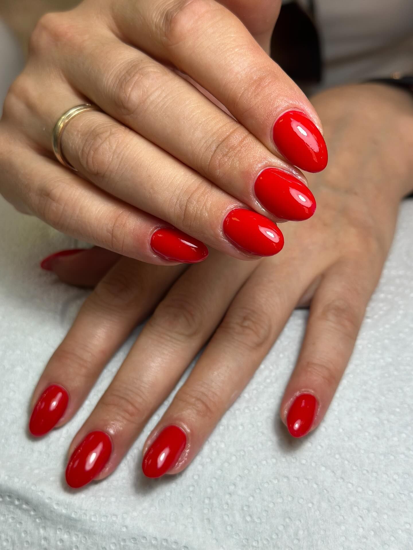 Manos con uñas rojas ovaladas y pulidas. Un anillo de oro en la mano izquierda.