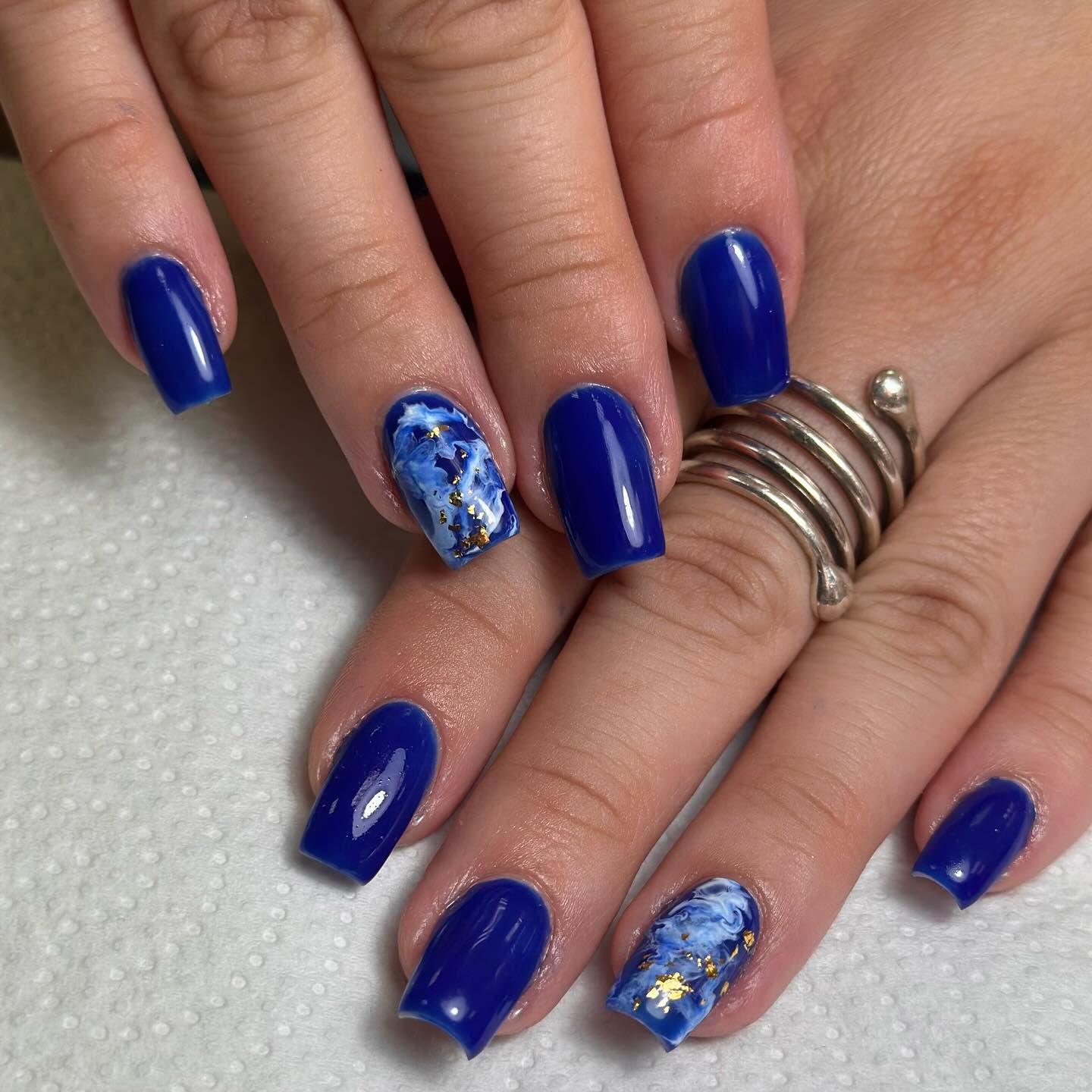 Manos con uñas decoradas en tonos azules y mármol, luciendo un anillo de plata.