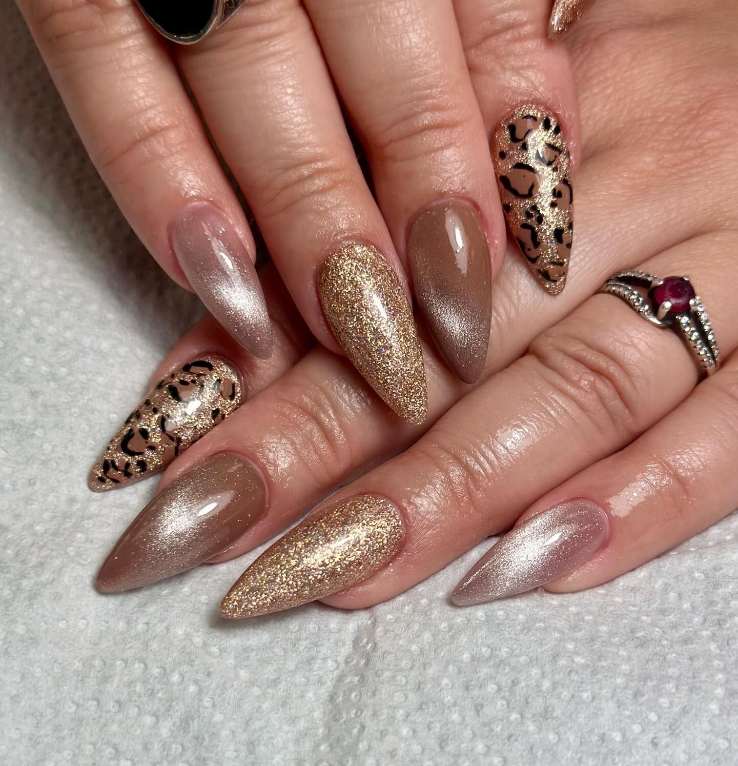 Uñas largas y puntiagudas con purpurina y estampado de leopardo, además de un anillo con un rubí.