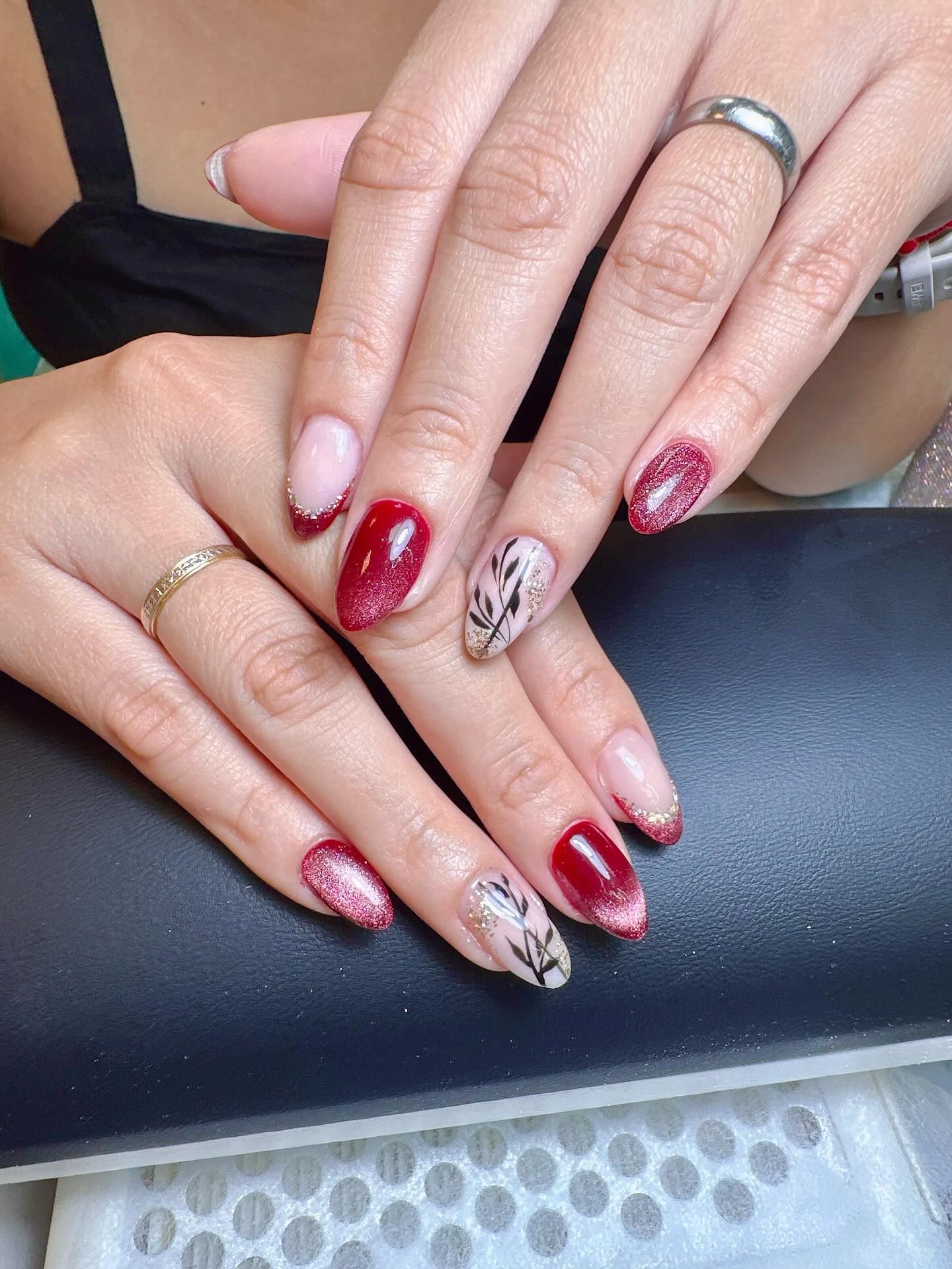 Manos de mujer con manicura. Diseño de uñas de gel rojo y rosa con purpurina y detalles florales.