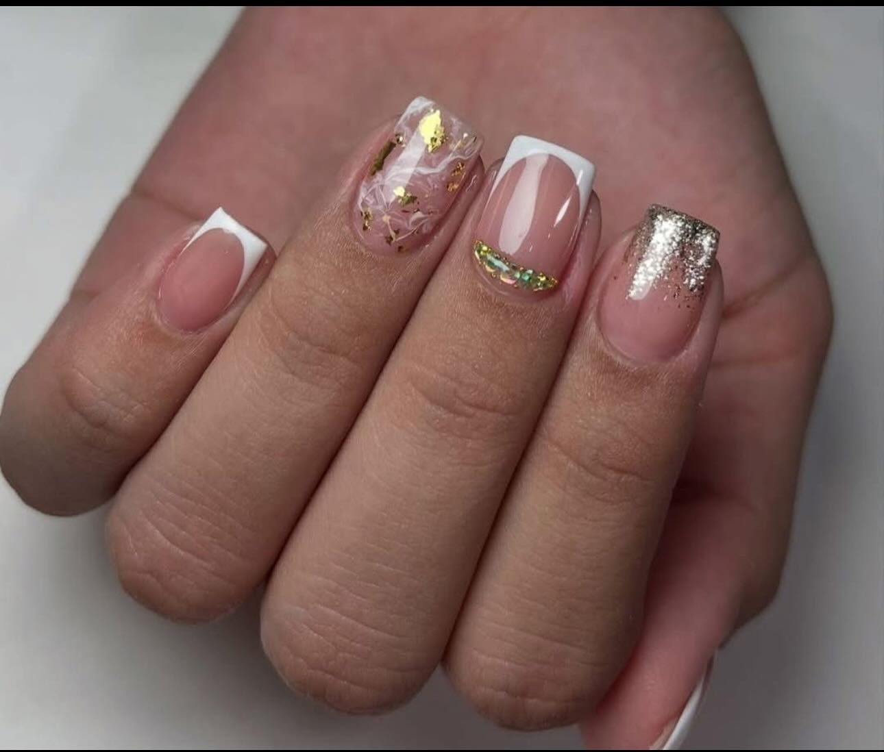 Primer plano de una mano con uñas de punta francesa, adornada con brillo dorado y detalles.