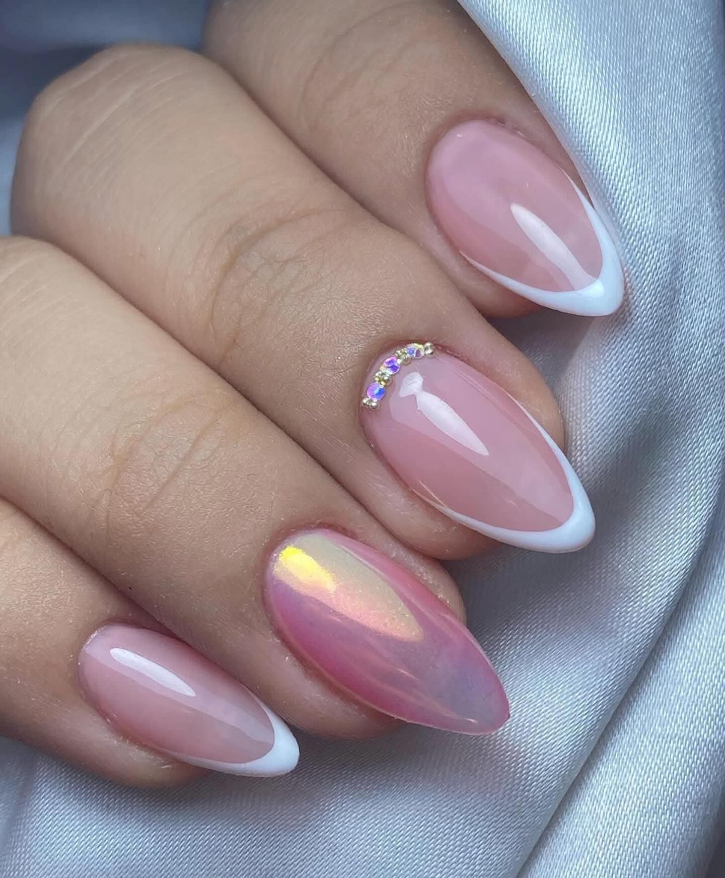 Mano con uñas de manicura francesa de forma ovalada, una uña acentuada con pedrería y rosa perlado.