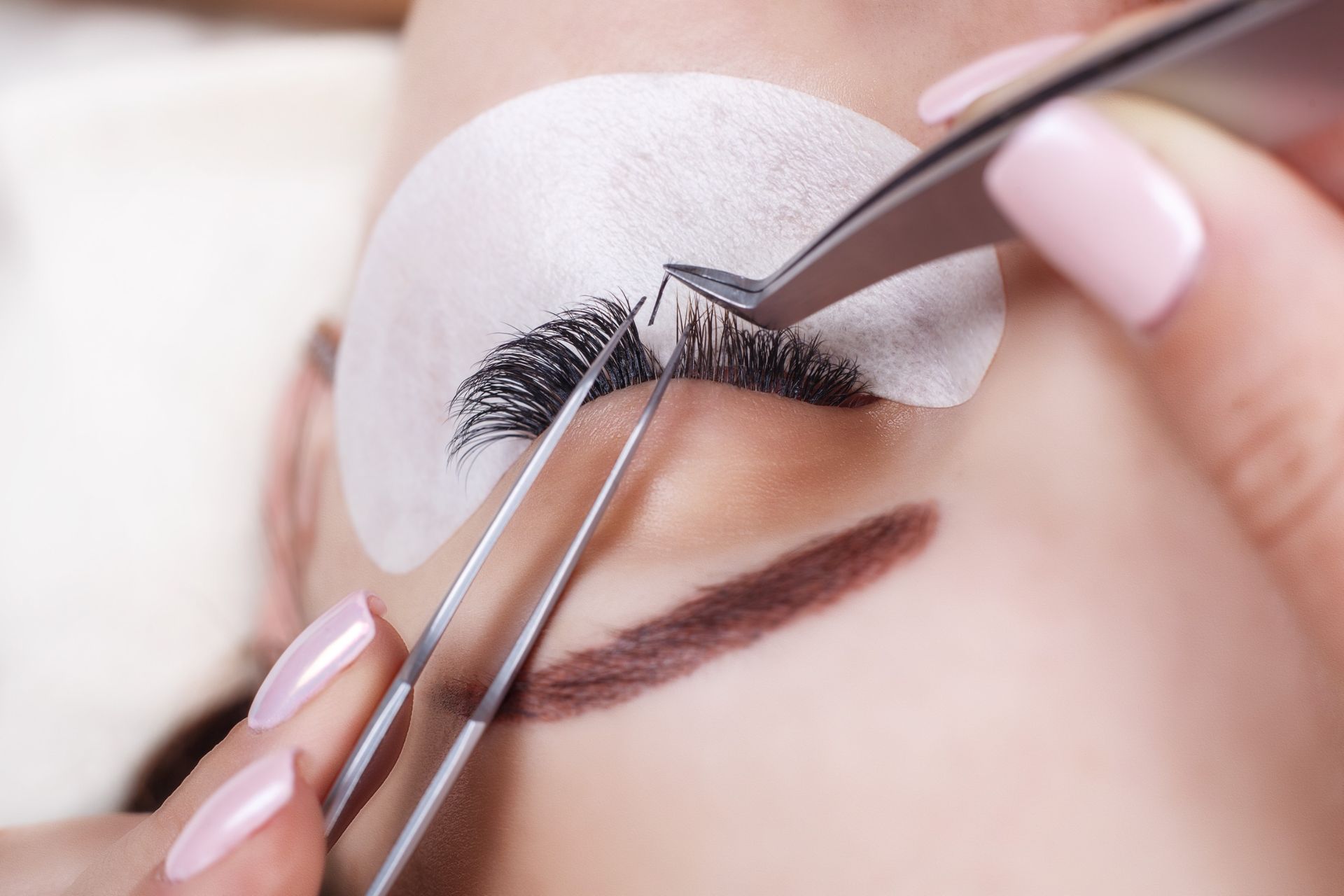 Mujer a la que le aplican extensiones de pestañas con pinzas.