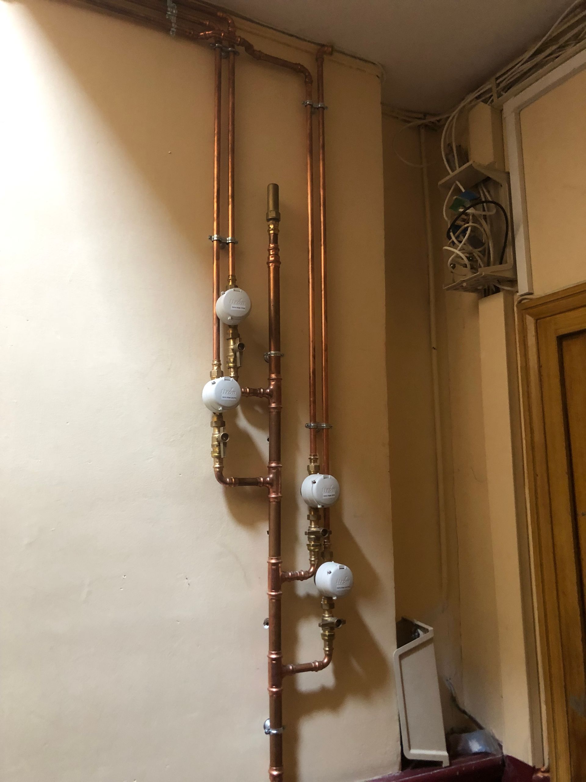 Tuyaux et manomètres en cuivre fixés sur un mur beige dans un couloir intérieur étroit