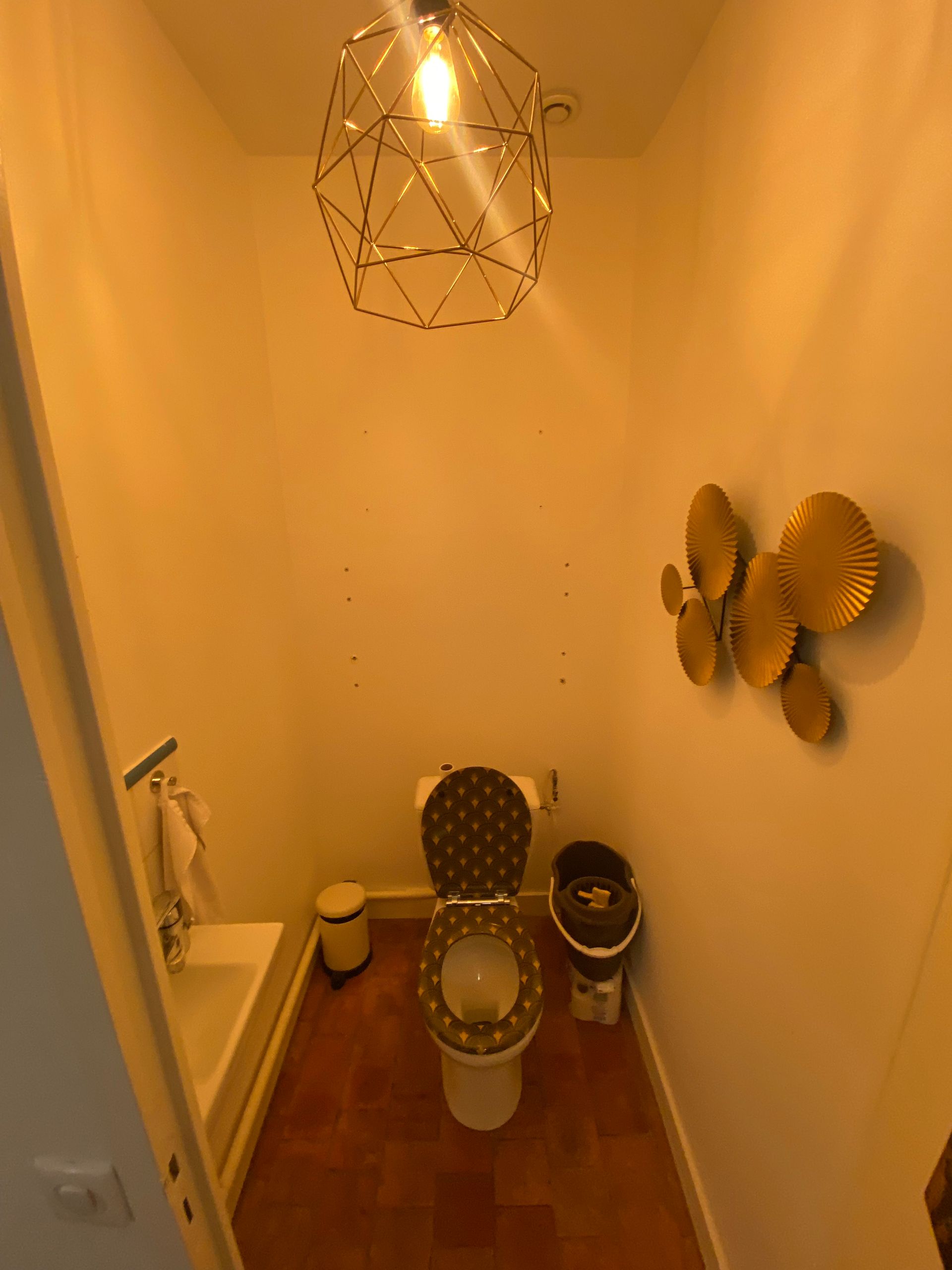 Petite salle de bains beige avec toilettes, lavabo et décoration murale, vue du dessus de la porte.