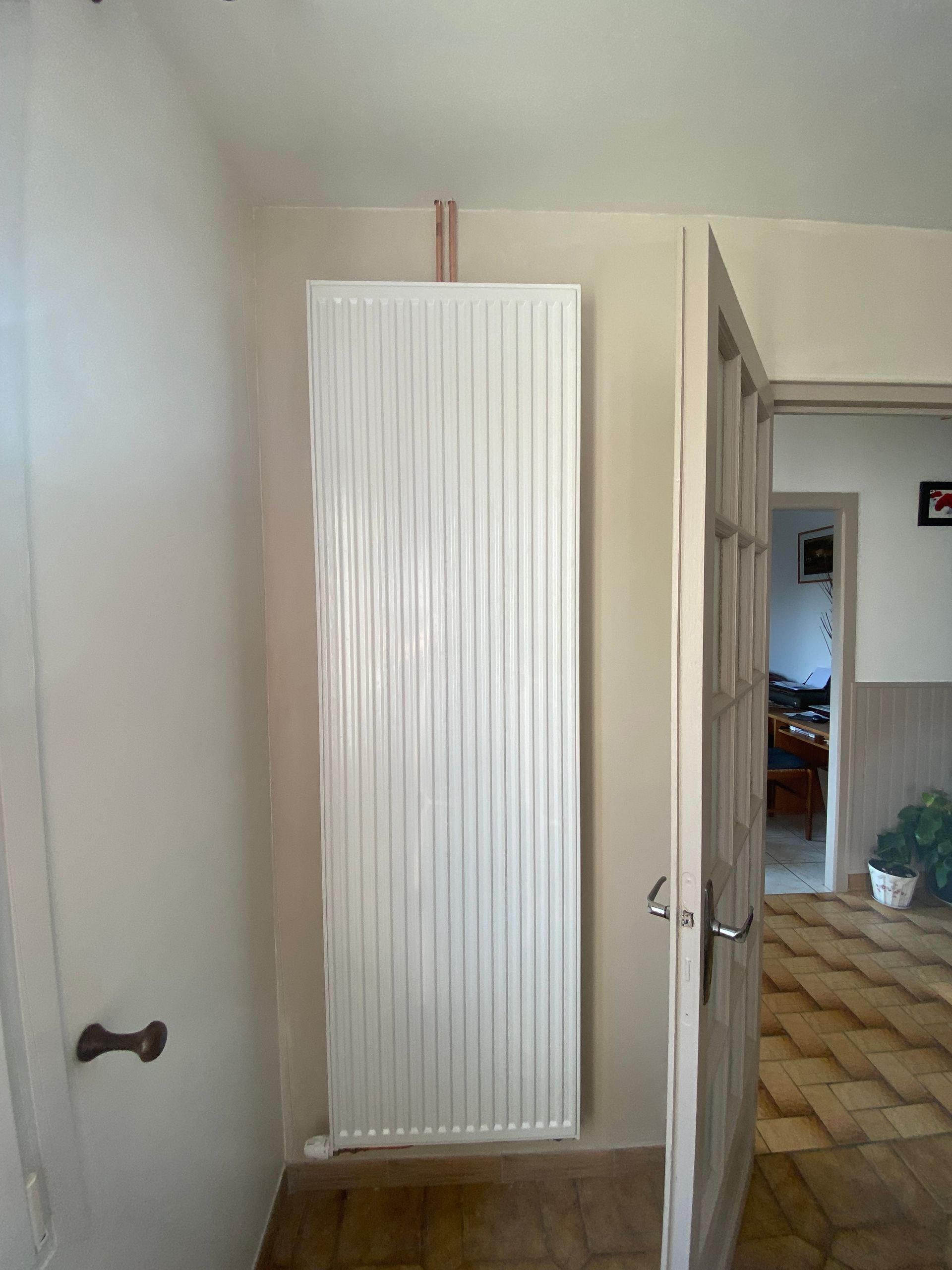 Couloir intérieur avec une porte ouverte, un radiateur blanc et un sol à motifs menant à une autre pièce
