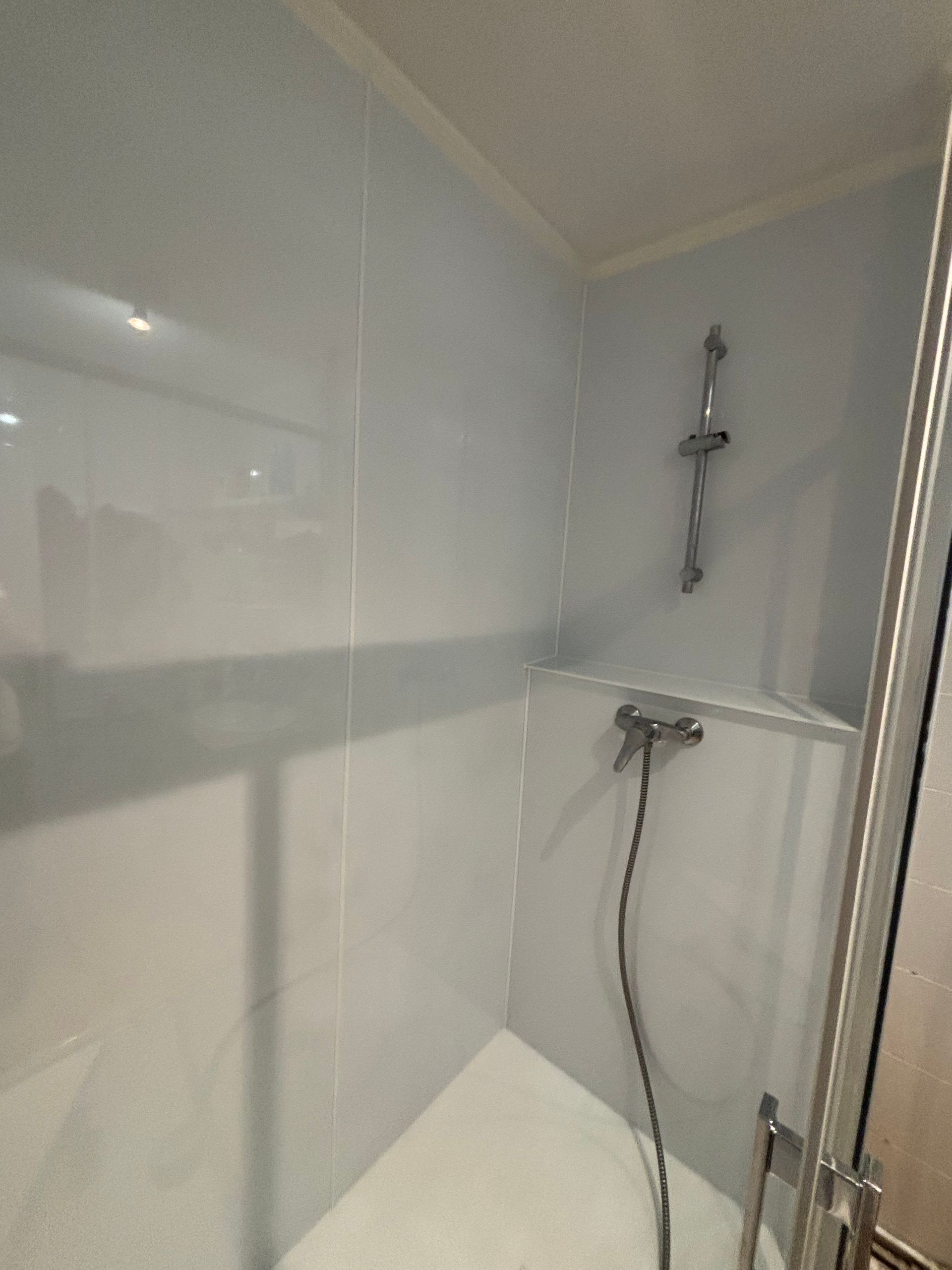 Petite cabine de douche carrelée blanche avec douchette et porte en verre.