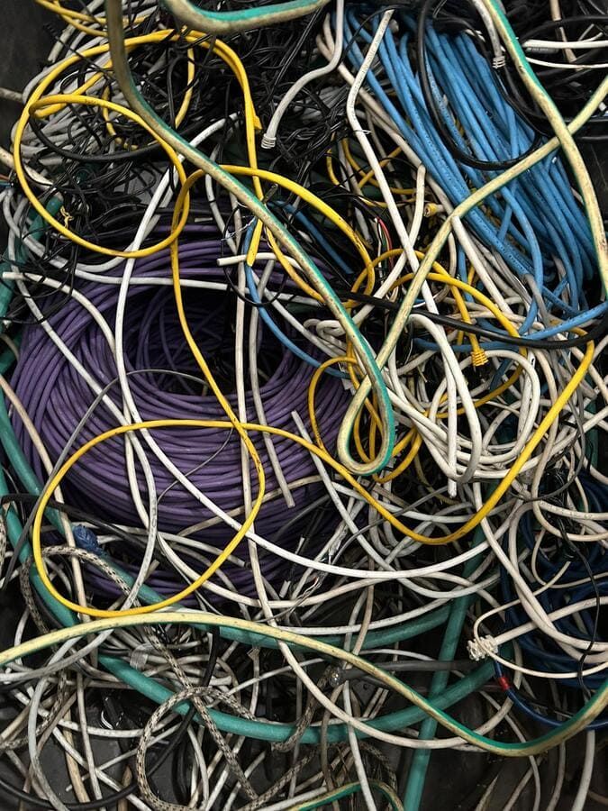 Surtido enredado de cables eléctricos de colores, incluidos azul, blanco, amarillo, morado y negro, probablemente desechados.