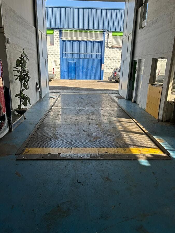 Vista desde el interior de un garaje hacia una puerta azul. En primer plano, un muelle de carga. El suelo es azul.