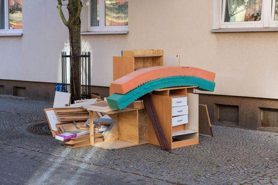 Des meubles en bois abandonnés et des morceaux de mousse entassés sur un trottoir à côté d'un bâtiment.