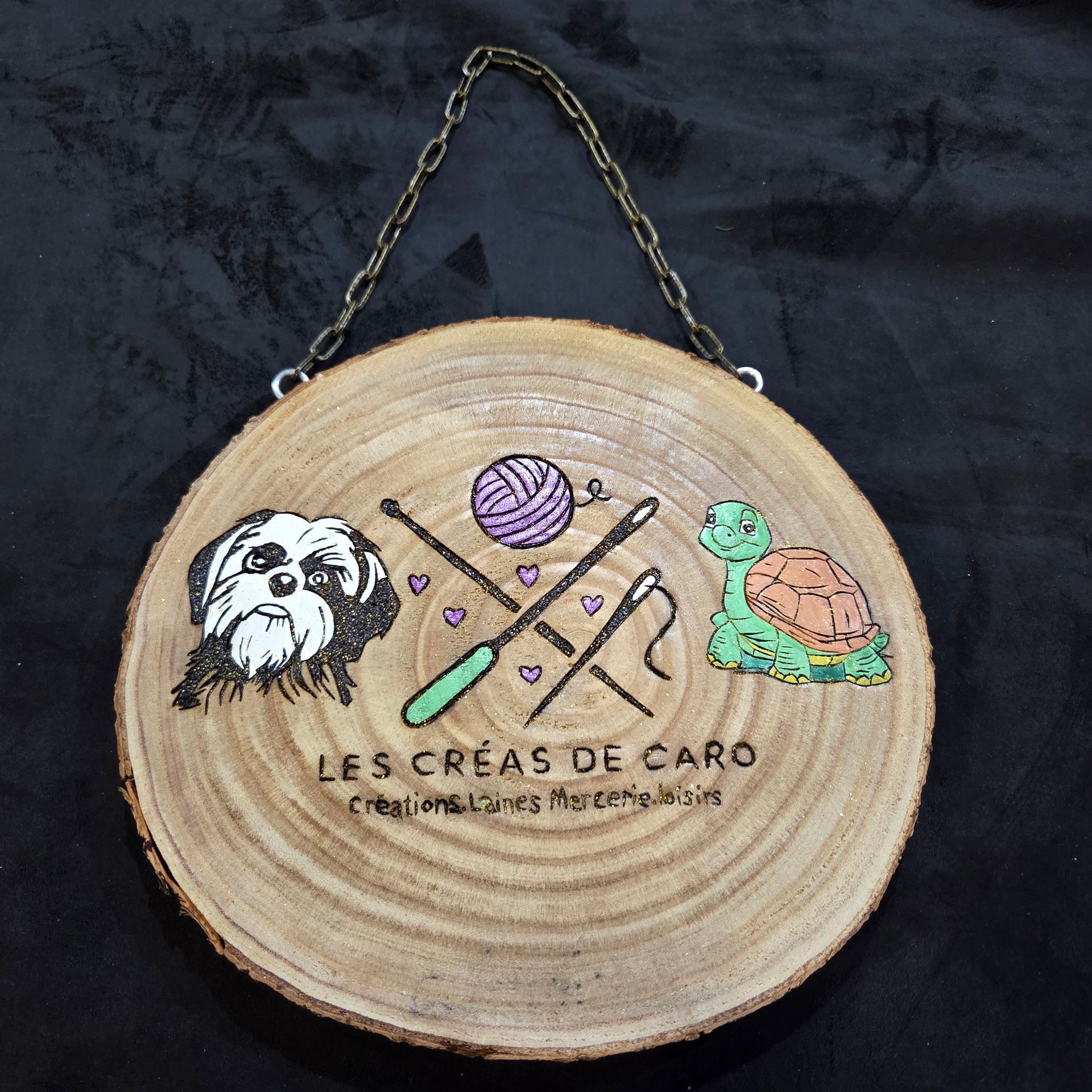 Une pancarte artisanale en bois représentant un chien, une tortue, de la laine et des outils de crochet avec le texte « LES CRÉAS DE CARO ».