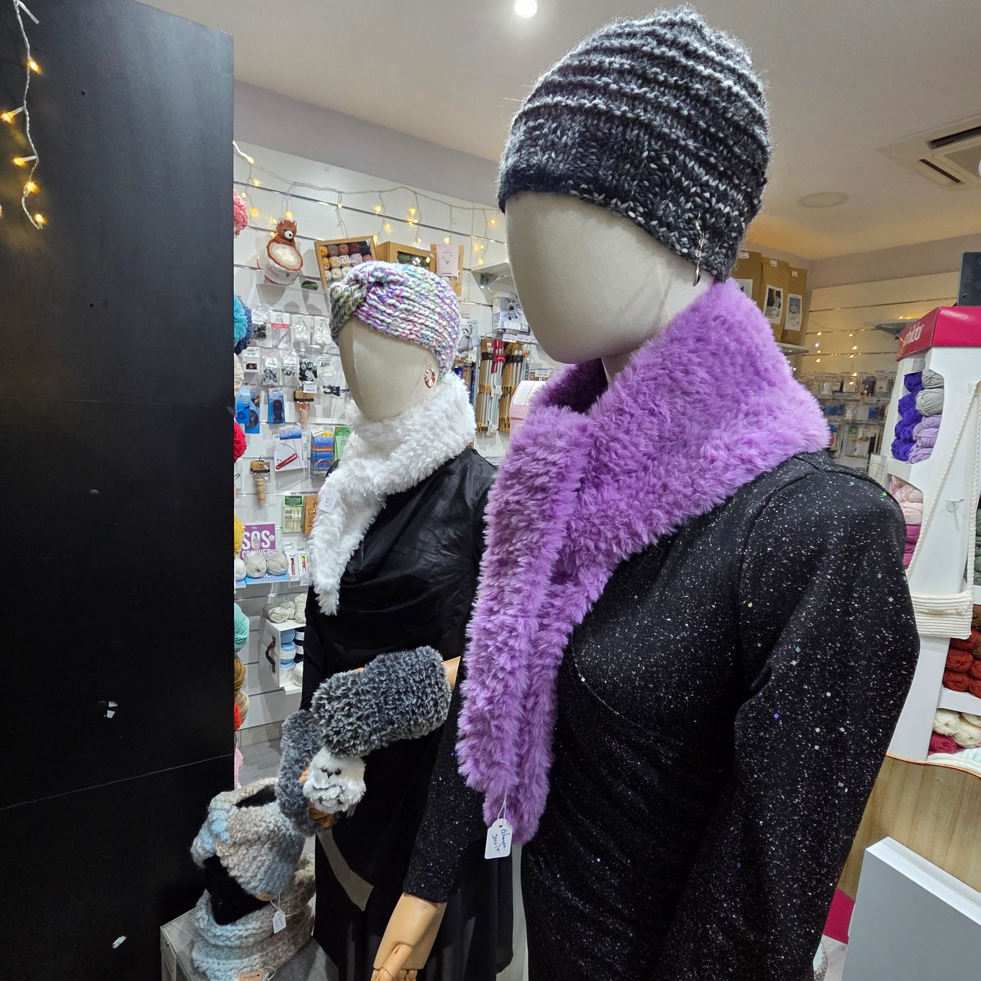 Deux mannequins exposés en magasin portent des bonnets d'hiver, des écharpes en fausse fourrure et des accessoires assortis.