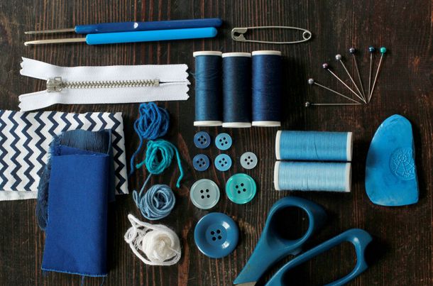 Fournitures de couture dans les tons de bleu, comprenant du fil, des aiguilles, des boutons, des chutes de tissu, des ciseaux et une fermeture éclair, le tout sur du bois.