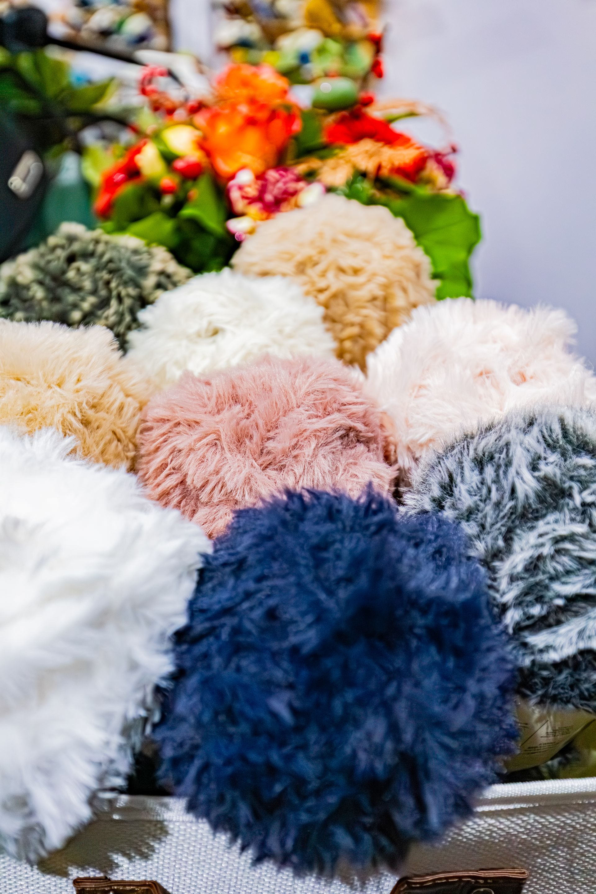 Un panier rempli de pompons colorés et duveteux de différentes nuances de bleu, rose, blanc, beige et vert foncé.