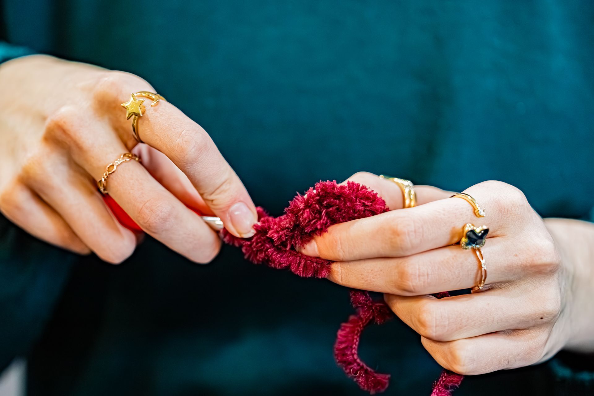 Mains avec des bagues, crochetées avec un fil duveteux rouge foncé sur un fond bleu sarcelle foncé.