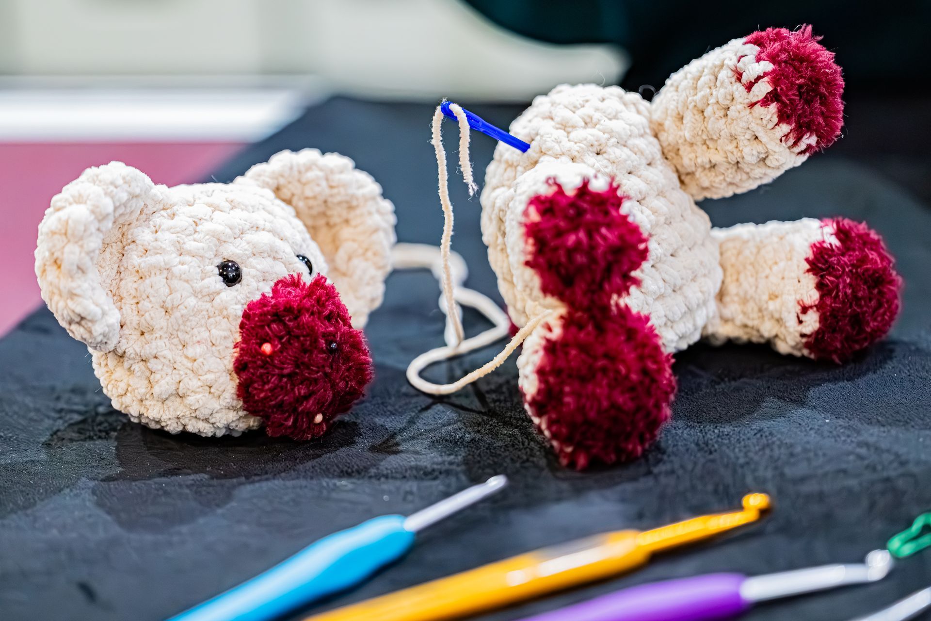 Une tête et un corps de koala au crochet, attendant d'être cousus ensemble avec une aiguille et du fil, avec des crochets au premier plan.