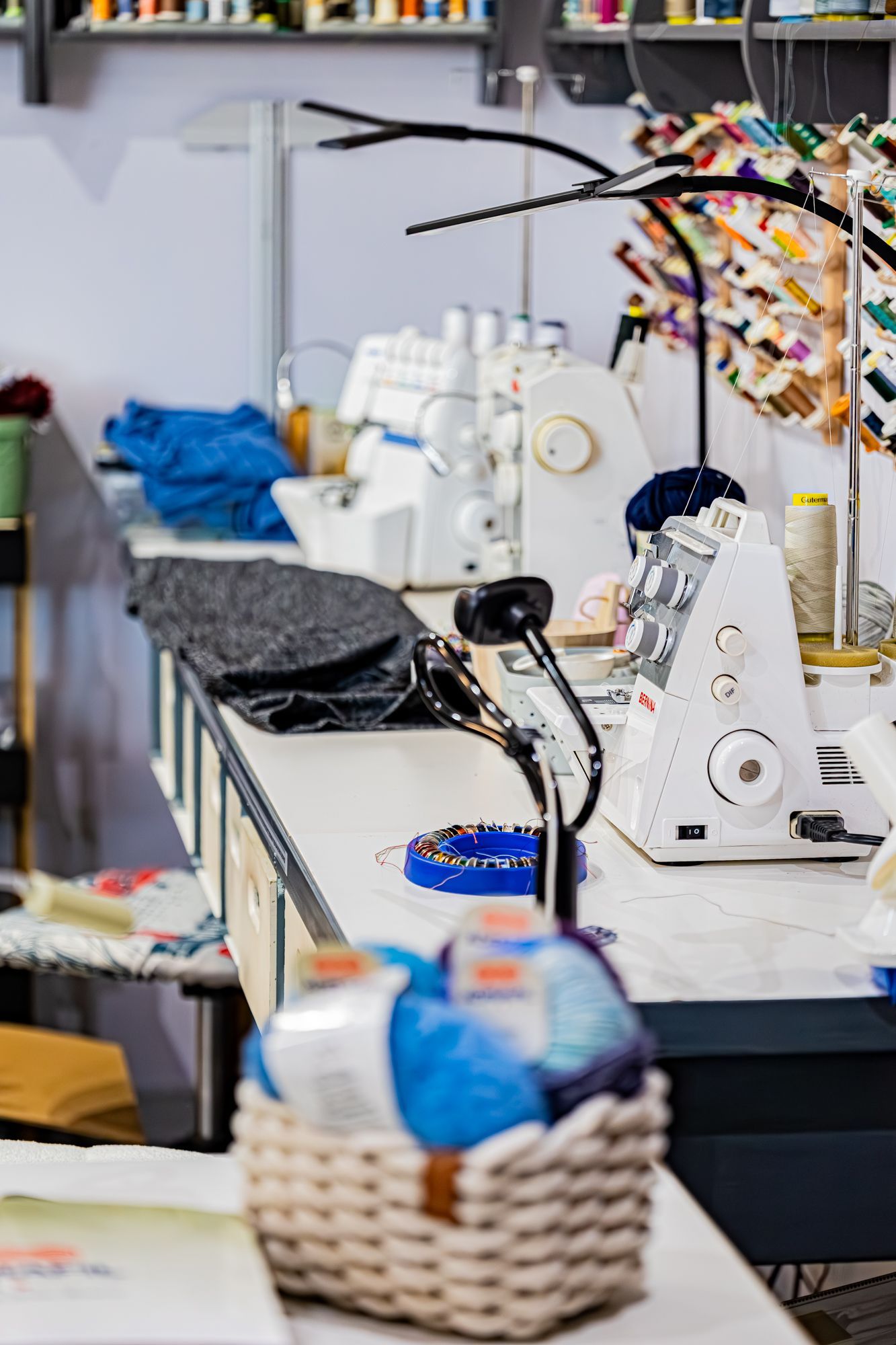 Une personne vêtue d'une chemise noire utilise un outil métallique pour ajuster un bouton sur un jean bleu à un poste de travail de machine à coudre.