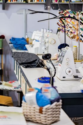 Une personne vêtue d'une chemise noire utilise un outil métallique pour ajuster un bouton sur un jean bleu à un poste de travail de machine à coudre.