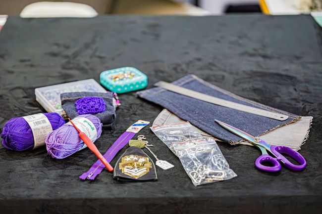 Matériel de loisirs créatifs, notamment du fil violet, un crochet, du tissu denim, des ciseaux et des articles de couture, sur une surface noire.