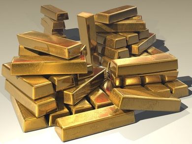Pila de lingotes de oro sobre una superficie neutra, de distintos tamaños y dispuestos de forma aleatoria.
