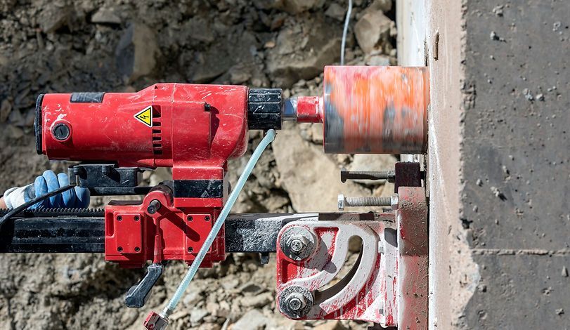 Rote Kernbohrmaschine auf einem Metallrahmen montiert, bohrt in eine Betonwand.