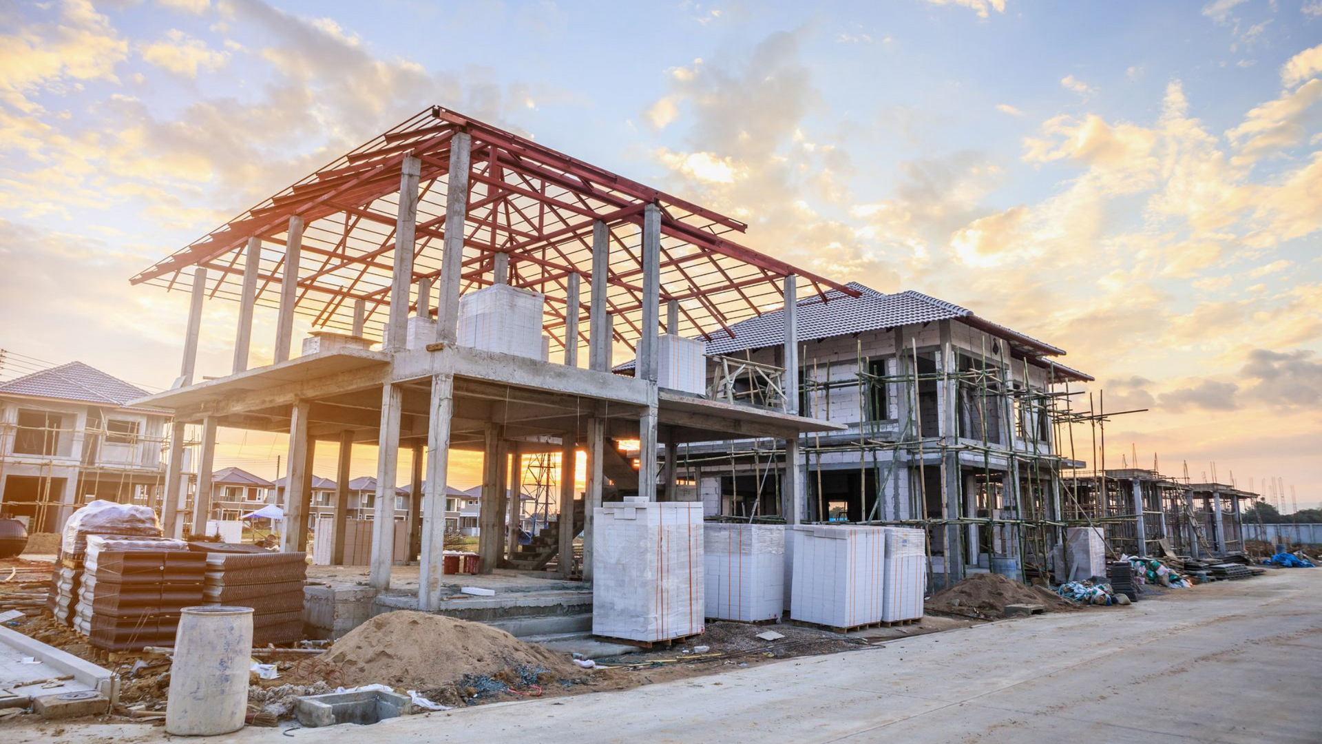 Maison en construction avec charpente et matériaux apparents au coucher du soleil.
