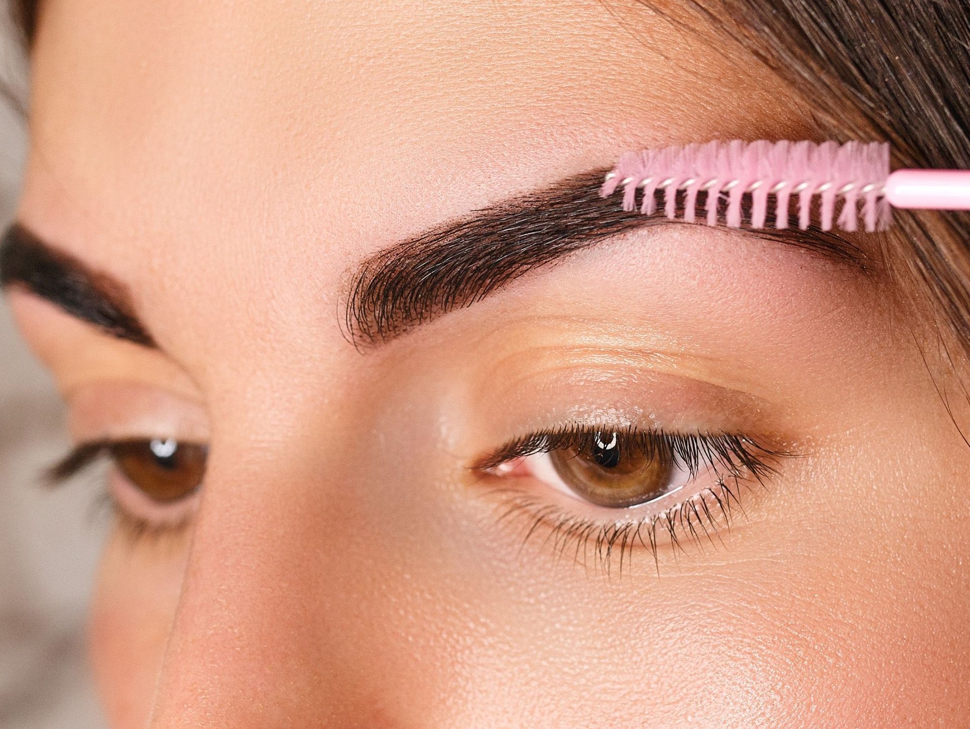 Una mujer se cepilla las cejas con un cepillo rosa.